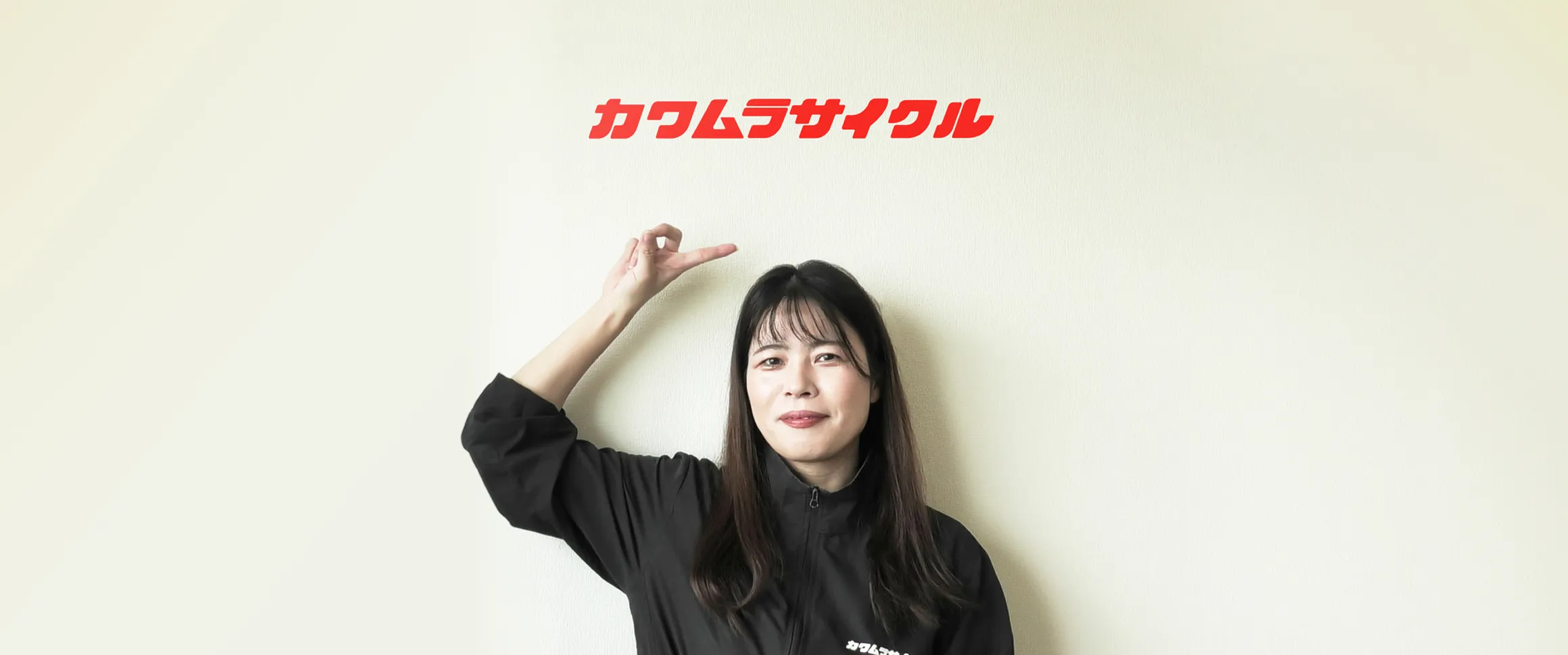 カワムラサイクルのロゴが掲げられた壁の前に立つ轟木有希様