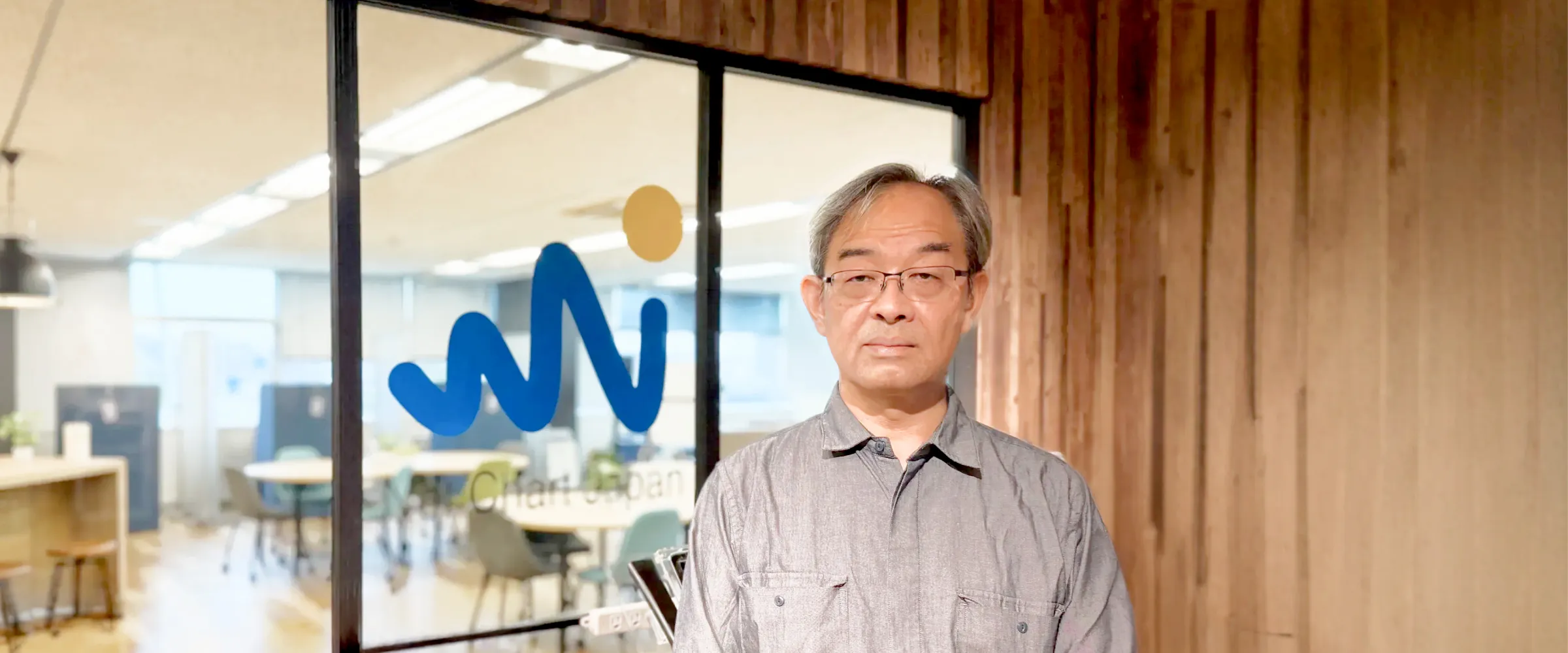 ネットチャート株式会社のオフィス入口のロゴ前に立つ丹野史明様