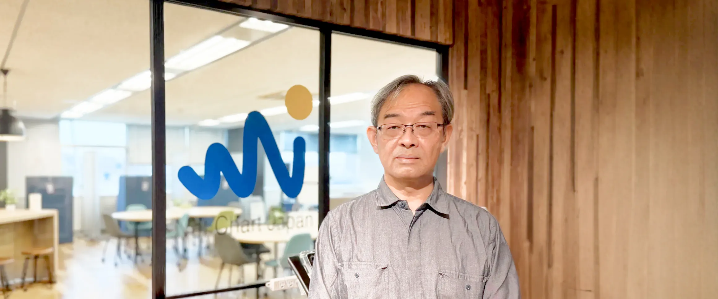 ネットチャート株式会社のオフィス入口のロゴ前に立つ丹野史明様