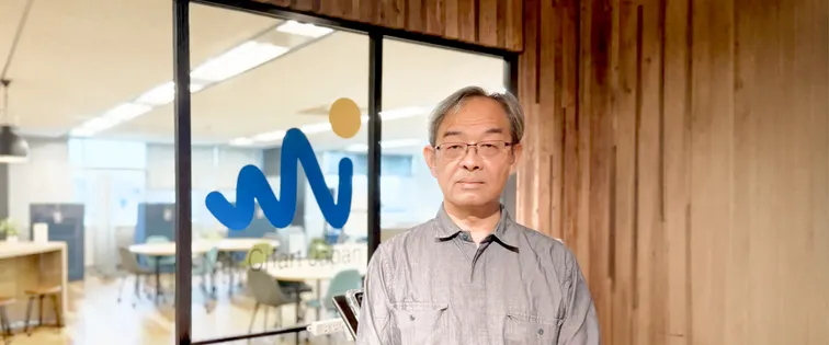 ネットチャート株式会社のオフィス入口のロゴ前に立つ丹野史明様