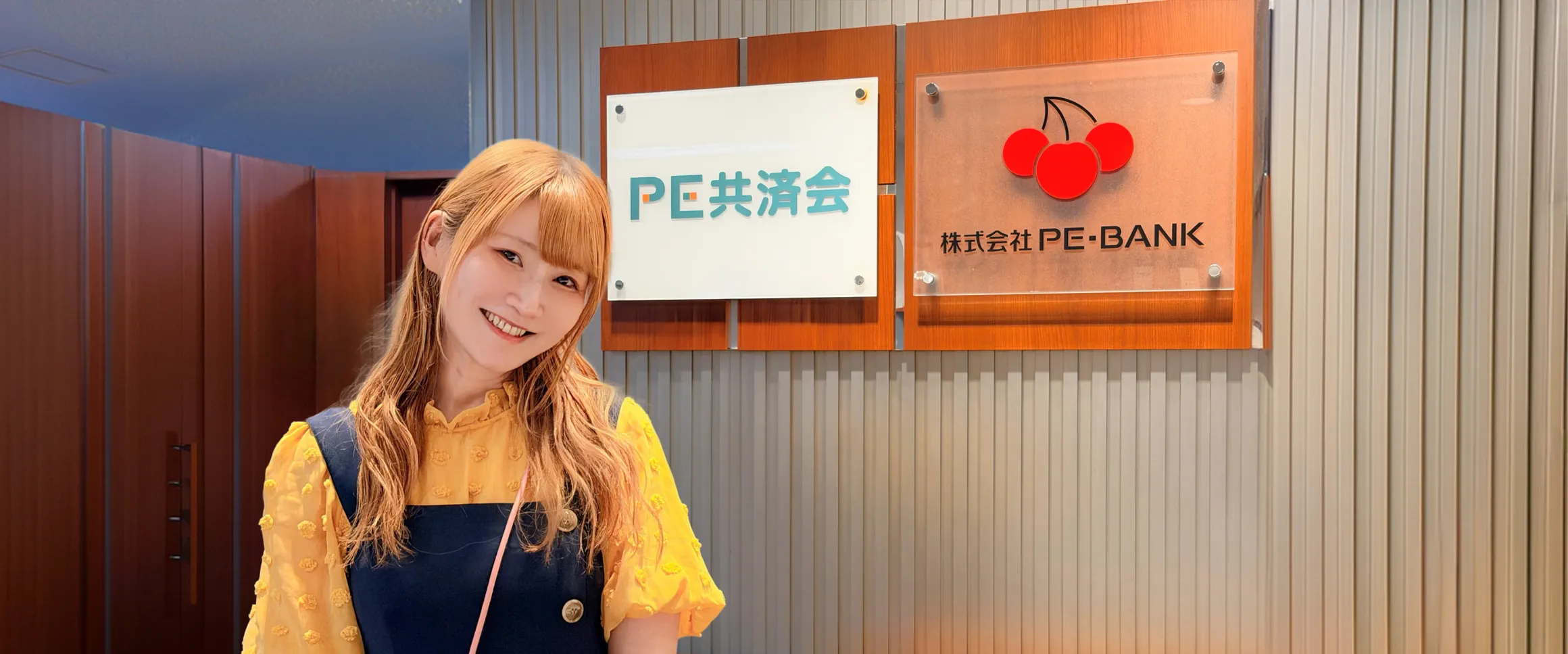 株式会社PE-BANKのサインボードの前に立つ福本麻実様